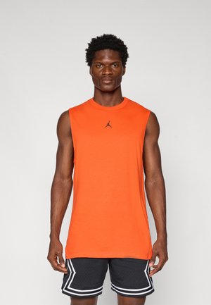 Un débardeur de sport orange sans manches avec un col rond et un logo noir sur la poitrine, associé à un short noir avec des accents blancs.