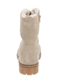 Bottines en suède beige avec doublure en fausse fourrure, semelle en caoutchouc robuste et fermeture éclair sur le côté. Présente des coutures décoratives et un logo.