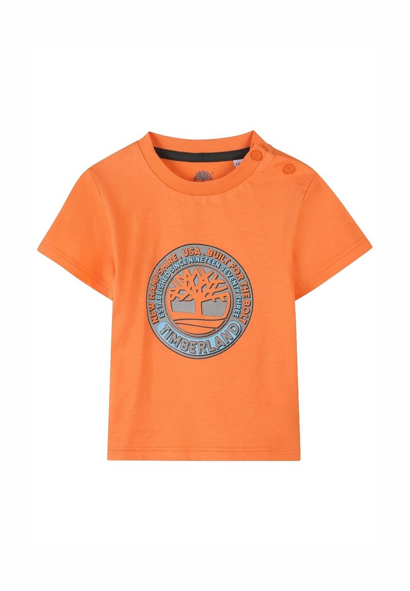 T-shirt arancione in cotone con maniche corte, caratterizzato da una grafica circolare del logo blu Timberland sul davanti e due dettagli a bottone sulla spalla.