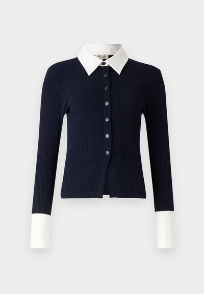 Marineblauwe geribde cardigan met een witte kraag, voorzien van een knopenlijst aan de voorkant en lange mouwen met witte manchetten. Textuurstof met een getailleerde pasvorm.