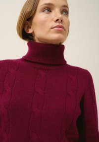 Bordowy sweter z golfem o wzorze w warkocze i ściągaczu, wykonany z miękkiego, teksturowanego materiału zapewniającego ciepło i komfort.