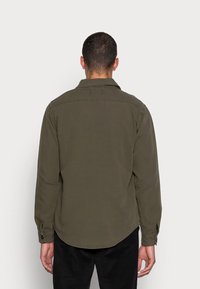 Camisa de manga larga color verde oliva, confeccionada con una tela suave. Presenta un cuello puntiagudo, puños con botones y dobladillo curvado. Vista trasera mostrada.