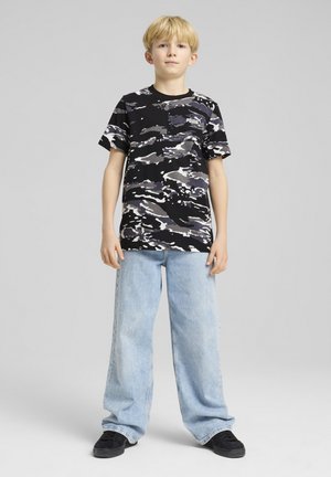 Camiseta de estampado de camuflaje en negro y gris con mangas cortas, combinada con jeans de mezclilla ligeros de corte holgado en azul claro y zapatos negros.