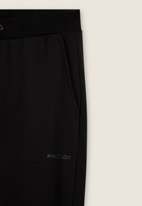 Pantalones de chándal negros con cintura elástica, bolsillo lateral y pequeño logo de Freddy cerca del bolsillo sobre un fondo claro.