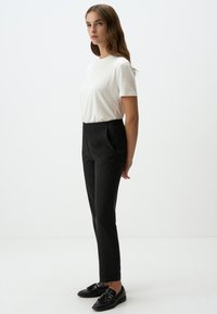 T-shirt bianco a maniche corte abbinato a pantaloni in vita neri a righe e mocassini neri, mostrato su un modello in piedi di lato.