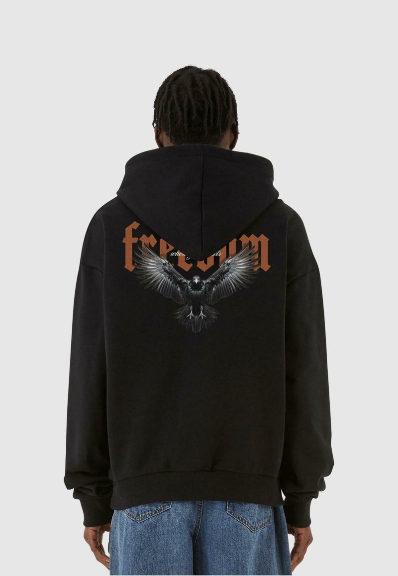 Felpa nera con cappuccio che presenta una grafica di un'aquila con le ali aperte e la parola "libertà" in arancione sul retro. Il materiale è morbido e texturizzato.