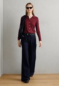 Camisa de botones de manga larga color burdeos con cuello, combinada con unos vaqueros de pierna ancha de color azul oscuro. Los accesorios incluyen unas gafas de sol negras y un bolso a rayas.