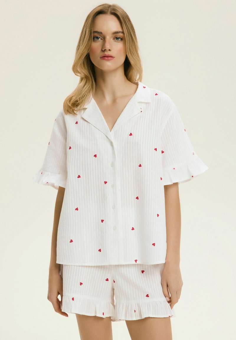 Biały bawełniany komplet piżamowy z krótkim rękawem, zapinany na guziki, oraz spodenki z falbankami, ozdobiony wzorem czerwonych serc i paskowanym wzorem.