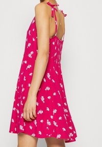 Robe d'été fleurie rose avec un corsage ajusté et une jupe évasée. Elle présente des bretelles réglables à nouer et un dos smocké pour un ajustement sûr.