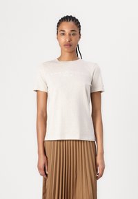 Bežinė medvilninė marškinėliai trumpomis rankovėmis, su balta "TOMMY HILFIGER EST. 1985" logotipu. Lygus paviršius ir laisvas pjūvis.