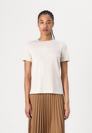 Beige cotton t-shirt with short sleeves, featuring "TOMMY HILFIGER EST. 1985" logo in white. Smooth texture and relaxed fit.