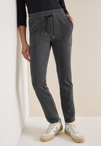 Grijze geweven joggers met elastische tailleband en trekkoord, voorzien van zijzakken en een taps toelopende pasvorm, gecombineerd met beige en blauwe sneakers.