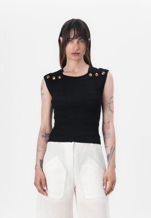 Black ribbed sleeveless top with a fitted design and gold button accents on the shoulders. Worn with white wide-leg trousers.