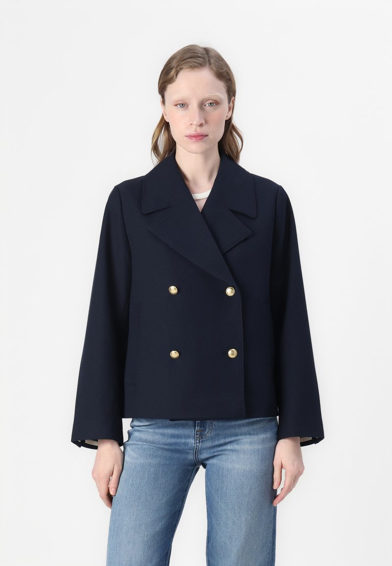 Marineblå dobbeltradet jakke lavet af struktureret stof, med store guldknapper og brede revers, parret med lyseblå denimjeans.