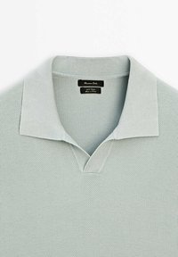 Polo gris clair en maille avec col ouvert et encolure en V, fabriqué en 100 % coton.