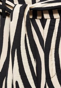 Detailní záběr na černobrou zdobenou látku se zebřími pruhy, s uzlem a viditelným švem.