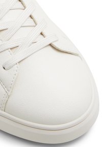 Sneaker in pelle bianca con lacci piatti, punta arrotondata, superficie texturizzata e dettagli di cucitura sottili. Design minimalista con una finitura pulita.