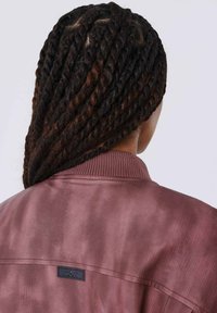 Donkerroze bomberjack met geribde kraag en zwart labeldetail. Glad textuur met een subtiele glans, gezien vanaf de achterkant.