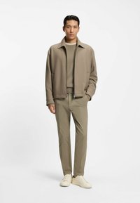 Helles Taubzip-Jackett über einem taupefarbenen Pullover, kombiniert mit schmal geschnittenen beigefarbenen Hosen und cremefarbenen Sneakern. Glatte Texturen und minimalistisches Design.
