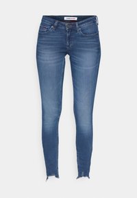 Jeans ajustados en denim de lavado medio. Presentan un dobladillo deshilachado, diseño clásico de cinco bolsillos y una etiqueta de marca en la cintura.