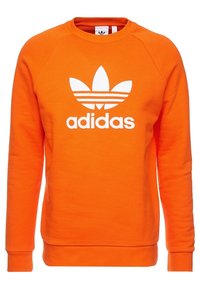 Oranžová mikina z měkké látky s bílým logem Adidas a designem tří pruhů na přední straně. Kulatý výstřih s žebrovanými manžetami.