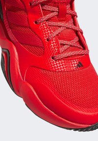 Roter Sportschuh aus Mesh und synthetischem Material, mit runder Zehenform, strukturiertem Obermaterial und kontrastierenden grauen Schnürsenkeln. Akzent aus schwarzem Gummi. 