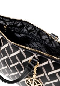 Sac à main noir et crème à motif avec fermeture éclair ; l'intérieur présente un tissu noir, plusieurs compartiments et des accents en métal doré.