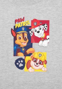 T-shirt grigia con personaggi di cartoni animati colorati di "Paw Patrol" con testo. I personaggi includono un cane in uniforme blu, un cane maculato e un cane con un cappello giallo.