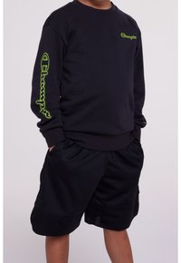 Black sweatshirt with neon green "Champion" logo on the sleeve, paired with black mesh shorts featuring pockets and a relaxed fit.