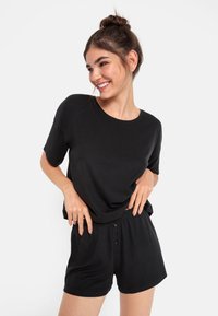 Svart kortärmad topp och matchande shorts i mjuk, ribbad tyg. Shorts med knapppartis på den elastiska midjebandet.