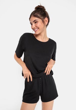 Svart kortärmad topp och matchande shorts i mjuk, ribbad tyg. Shorts med knapppartis på den elastiska midjebandet.