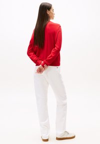 Maglione rosso con scollatura rotonda e maniche lunghe, abbinato a pantaloni bianchi a gamba dritta e sneakers chiare, visto da dietro.