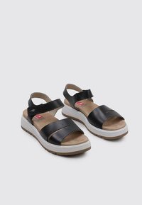 Sandalias de cuero negro con dos correas anchas, plantilla acolchada y suela de goma blanca. Incluye una correa ajustable en el tobillo.