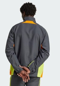 Grijze sportjack met oranje en neongroene accenten, hoge kraag en elastische boorden; beschikt over een relaxte pasvorm en een gladde textuur.