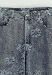 Jeans en denim gris avec un motif floral dans une teinte plus claire. Comprend des poches latérales et une fermeture par bouton en métal à la taille.