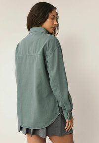Verbleekte groene denimhemd met een kraag, lange mouwen en een gebogen zoom. Heeft een knoopsluiting bij de manchetten en een effen structuur.