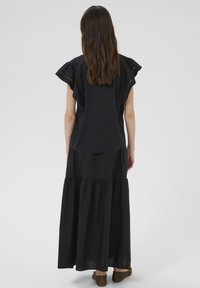 Sort bluse med flæseærmer, parret med en lang sort lagdelt nederdel. Blødt stof, flydende design, knælang kant og strukturerede detaljer.