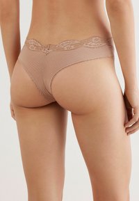 Beige ondergoed met kanten rand, voorzien van verticale ribbels, met een lage taille en een gegolfde rand langs de tailleband en beenopeningen.