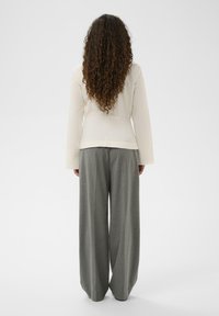 Kreem värvi pikad varrukad pluus, millel on kitsas talje ja lahtine seljaosa, kombineeritud laia jalaga hallide triibuliste pükste kanssa, millel on sile tekstuur.