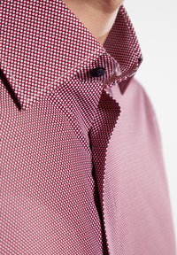 Rood en wit gestreepte shirt met een gestructureerde stof. Beschikt over een gestructureerde kraag en donkere knoopdetails.