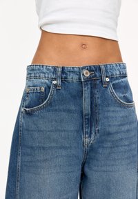 Blugi din denim albastru cu talie înaltă, având închidere cu nasture, bucle pentru curea și un design clasic cu cinci buzunare. Textură uzată în țesătură.