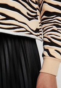 Beige och svart randig stickad topp med vita accenter, kombinerad med en veckad svart kjol. Mjuk textur, avslappnad design, fållen slutar vid midjan.