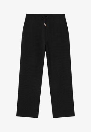 Czarne spodnie szerokie z elastycznym paskiem w talii i sznurkiem z metalowymi, złotymi końcówkami, na jednolitym tle.