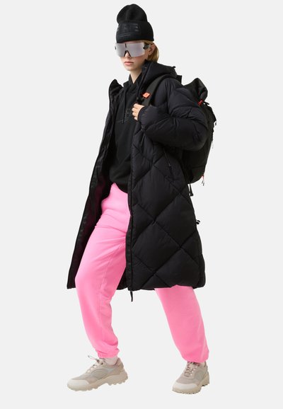 Zwarte donzen jas met diamantenquilt, roze joggingbroek, beige sneakers en een zwarte muts; reflecterende zonnebril; casual stedelijke stijl.