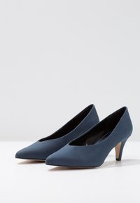 Chaussures à talons hauts en daim bleu avec bout pointu, côtés échancrés et talon effilé. Texture lisse et design minimaliste.