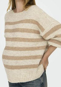 Beige a krémový pruhovaný pletený svetr s kulatým výstřihem a krátkými rukávy; měkká textura a volný střih, s ribovanými lemy a bočními rozparky.