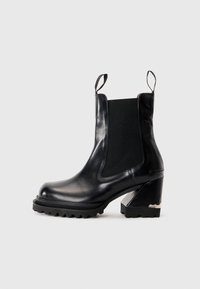 Botte de cheville en cuir noir avec un talon chunky, semelle striée, panneaux élastiques sur les côtés et languettes au niveau de la languette et du talon.