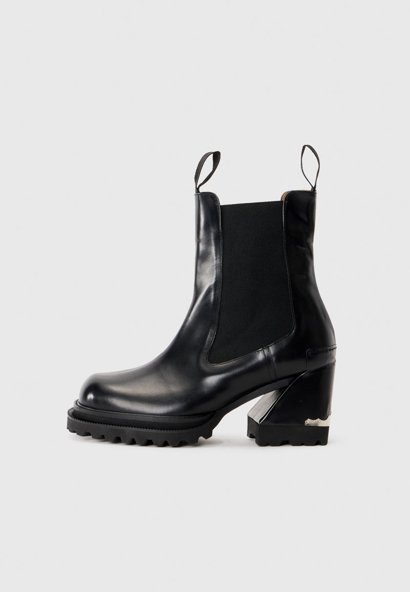 Botte de cheville en cuir noir avec un talon chunky, semelle striée, panneaux élastiques sur les côtés et languettes au niveau de la languette et du talon.