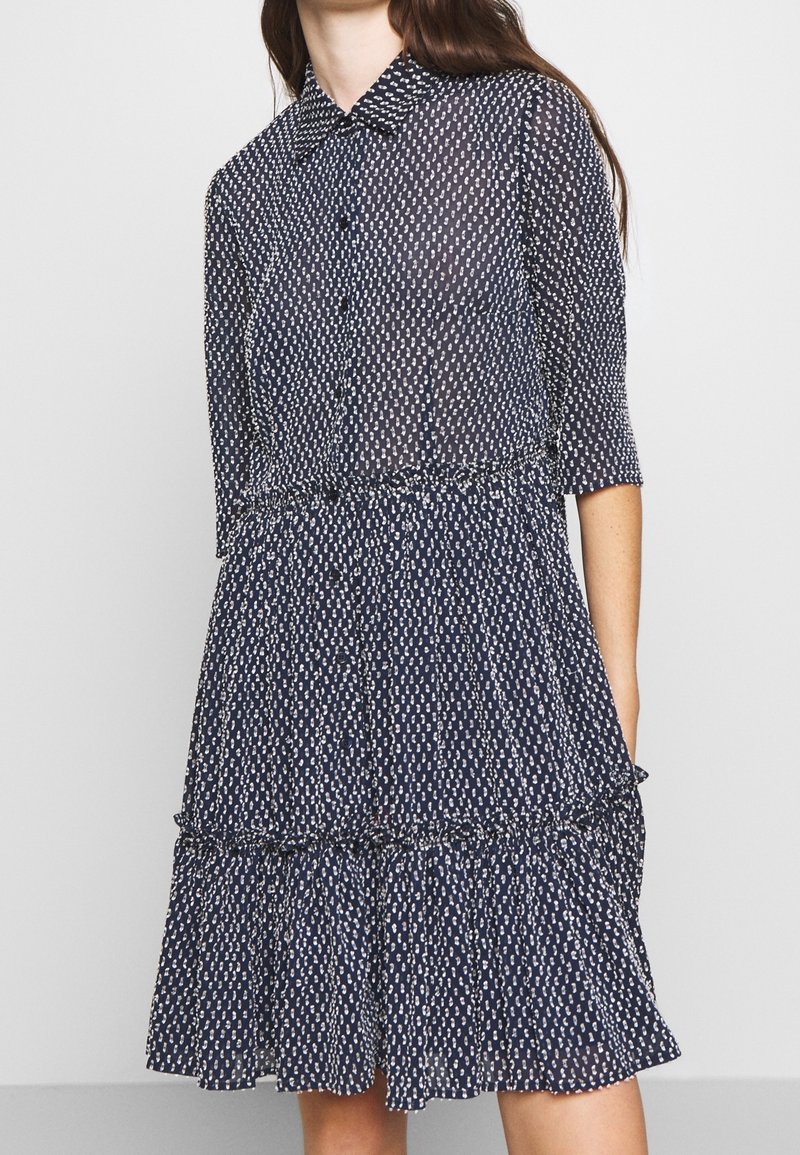 Mörkblå klänning i genomskinligt tyg, med ett prickigt mönster, knappstängning framtill, krage och ett flerlagers volangslut med trekvartslånga ärmar.