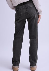Jeans de mezclilla en gris oscuro, con un corte relajado, diseño de cinco bolsillos, costuras visibles y dobladillos deshilachados en los tobillos.